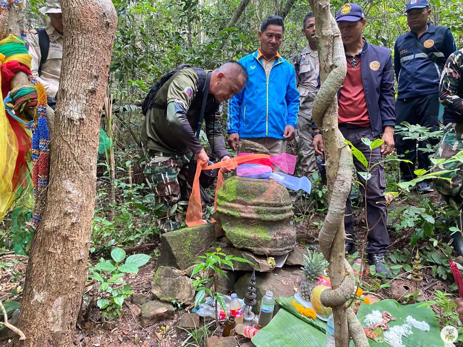 กลุ่มผู้ร่วมลงพื้นที่อยู่ใกล้ชิ้นส่วนหินและผ้าสี ภาพกิจกรรมปัจจุบันไม่ใช่หลักฐานยืนยันพิธีกรรมในอดีต